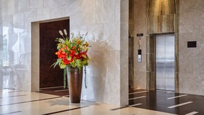 Eine moderne Lobby mit Marmorboden, einer großen Blumenvase und einem Aufzug.