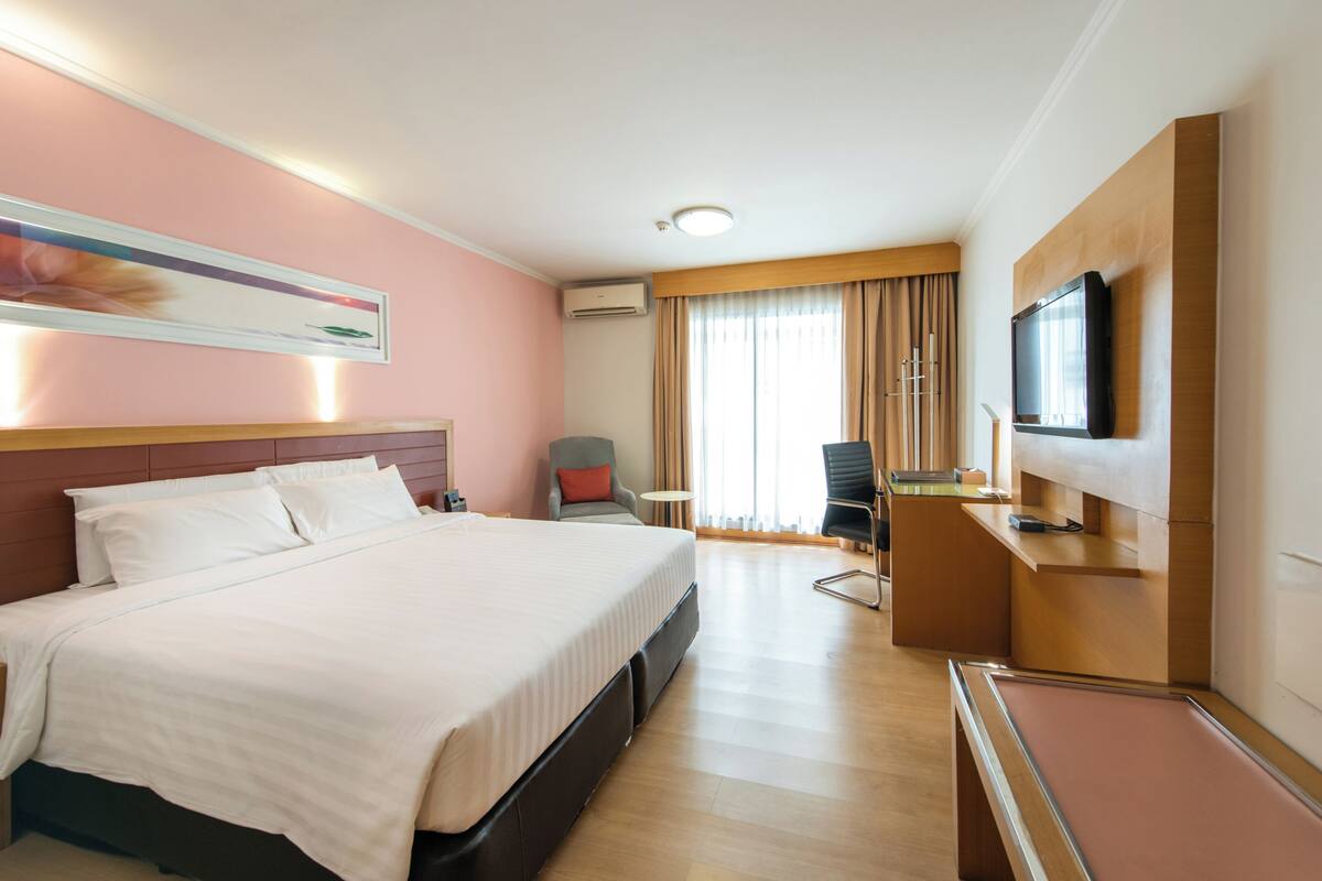 A hotel room with a large bed, a desk, a chair, a television, and a window with curtains.