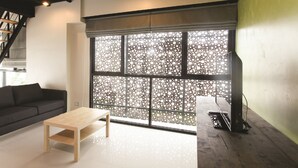 Una sala moderna con una mesa de centro de madera, un sofá negro y un ventanal con un panel decorativo.