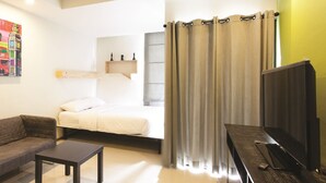 Un espacio habitable compacto con cama, sofá, una mesita y televisor.