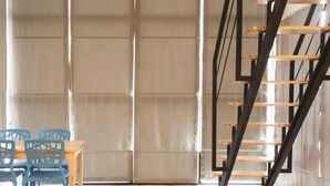 Un interior moderno con una escalera, una mesa con sillas y un ventanal grande.