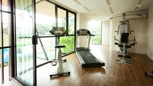 Un gimnasio moderno con caminadora, elíptica y máquinas de pesas, ventanas amplias con vistas a zonas verdes.