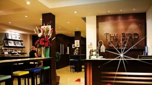 A reception area with a wooden counter, a sign reading "The Bird Cafe," and a bar area with stools. - The Bird Cage Patong Guesthouse (Kathu)