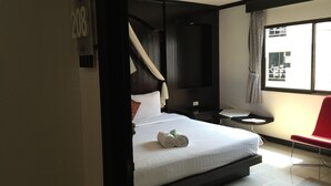 A modern hotel room with a large bed, a small bedside table, a chair, and a view of the outside. - The Bird Cage Patong Guesthouse (Kathu)
