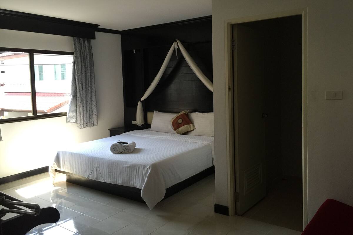 Een hotelkamer met een bed, nachtkastje, raam met gordijnen en een deur.