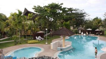 Uma área de piscina em resort com hidromassagem, espreguiçadeiras e um jardim tropical.