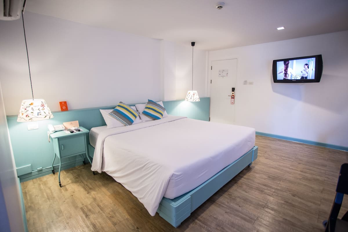 A bedroom with a bed, a nightstand, a lamp, a TV, and a wooden floor.