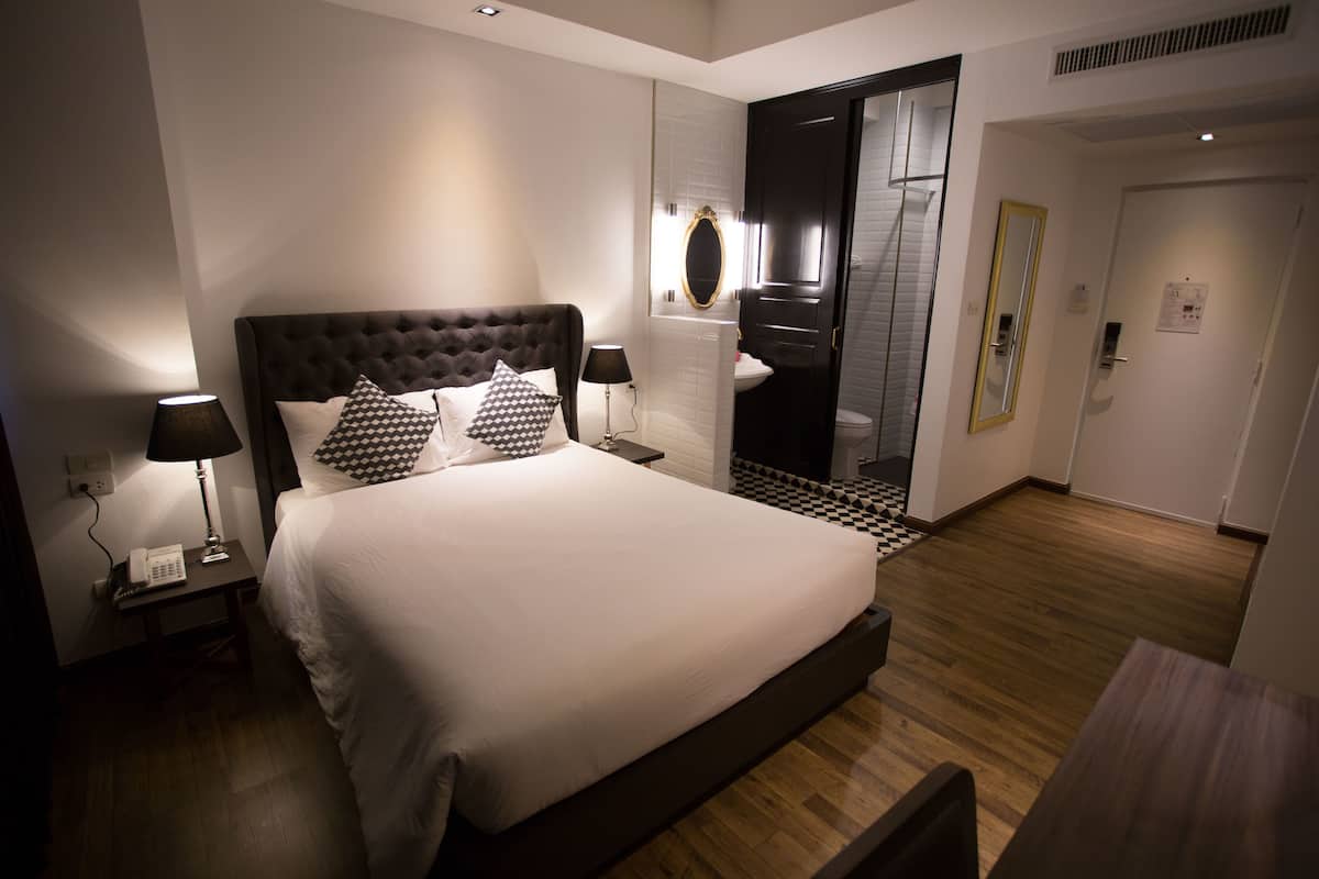 A modern hotel room with a large bed, bedside lamps, a mirror, and a wooden floor.