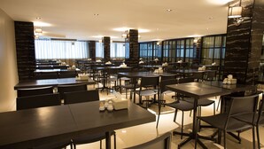 Un restaurante moderno con varias mesas y sillas, ventanas amplias con cortinas y una pared de acento de mármol.