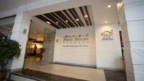 Entrada de hotel con diseño moderno, un cartel visible que dice "First House Bangkok" y un área de recepción a la vista.