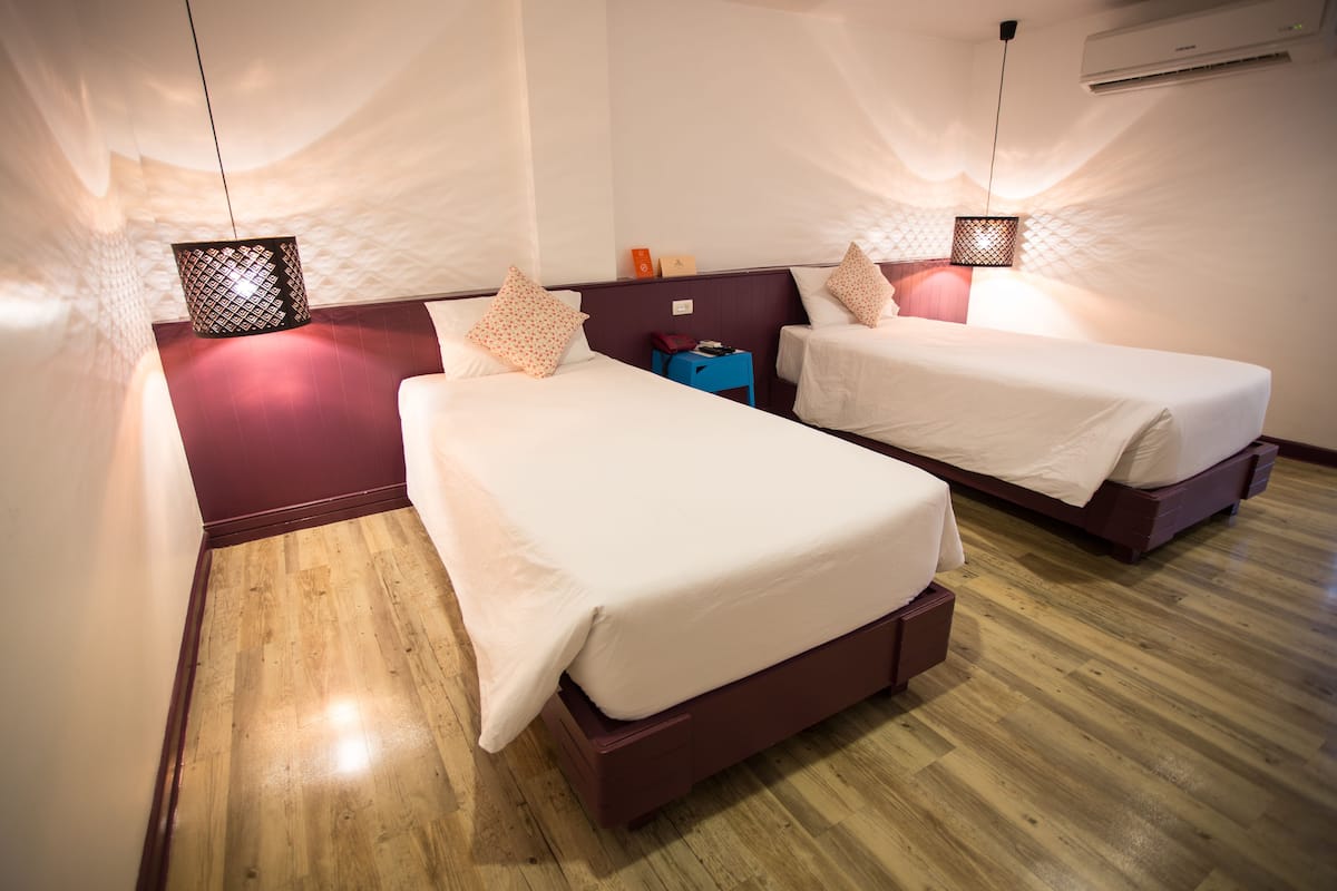 A hotel room with two beds, a wooden floor, and a headboard with a built-in shelf.