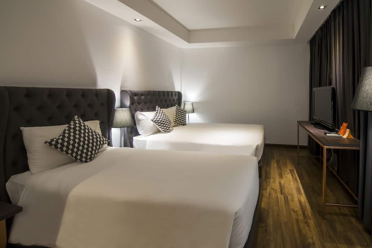 A modern hotel room with two beds, a television, and a desk with a lamp.