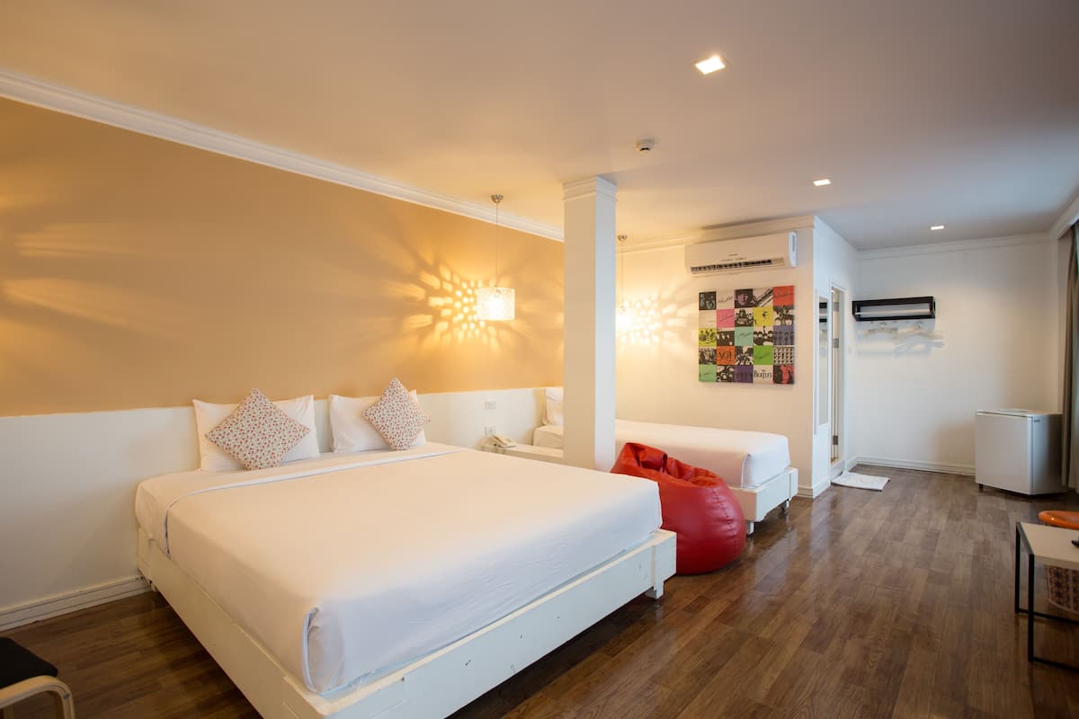 A hotel room with a large bed, a red bean bag chair, a small table, and a wall-mounted air conditioner.