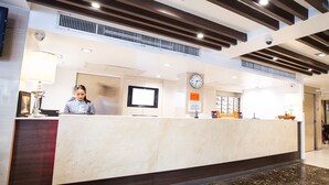 Zona de recepción de un hotel con mostrador de mármol, un reloj y una televisión.
