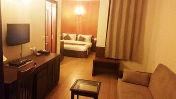 A hotel room with a TV, a sofa, a coffee table, and a bed.