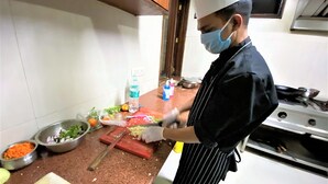 A chef preparing food in a kitchen with a cutting board, vegetables, and a water bottle. - Tavisha Villa (Gurugram)