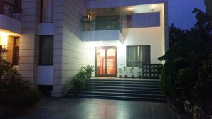 A modern two-story building with a glass door entrance, steps leading up to the door, and potted plants around the entrance. - Tavisha Villa (Gurugram)