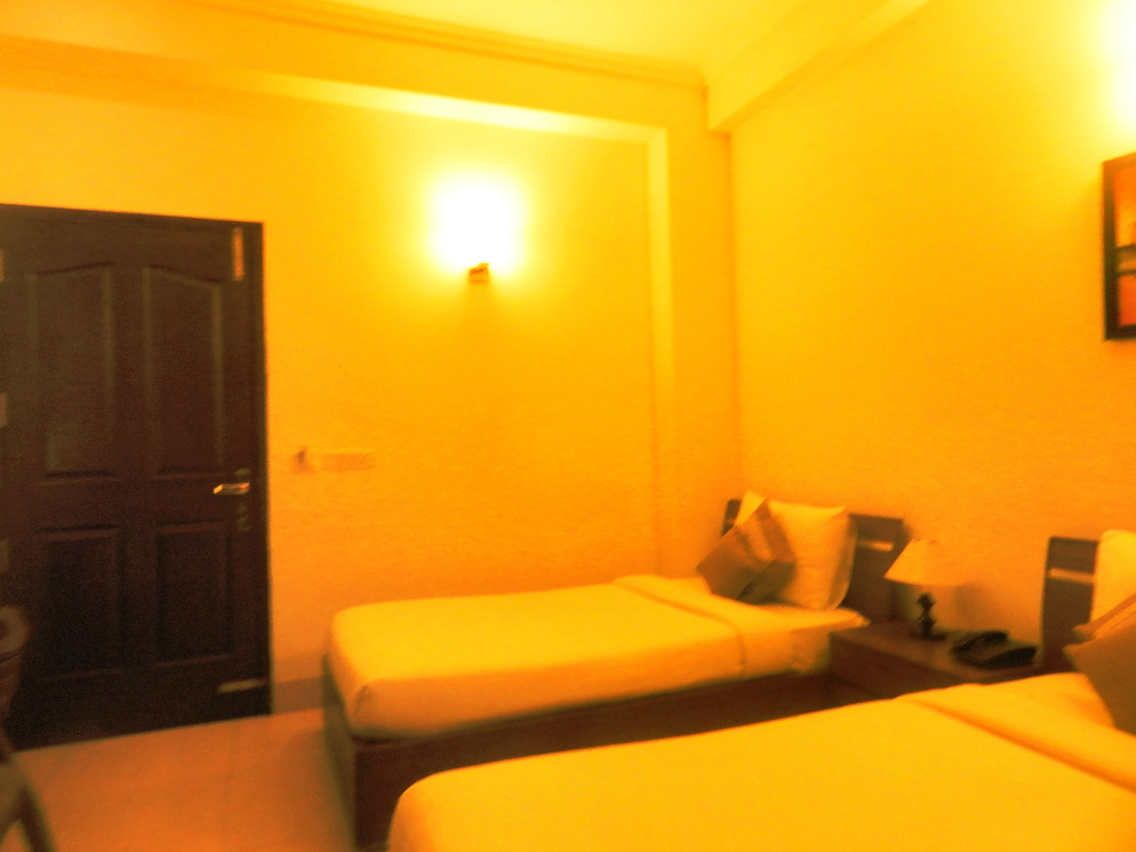 Una habitación de hotel con dos camas individuales, una mesita de noche con lámpara y una puerta.