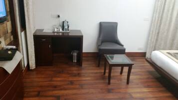A compact room with a wooden floor, a desk with a chair, a small glass table, and a bed.