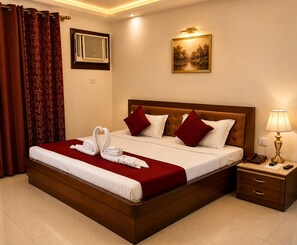 Habitación de hotel con una cama grande, una mesita de noche con lámpara, un cuadro en la pared y una ventana con aire acondicionado.