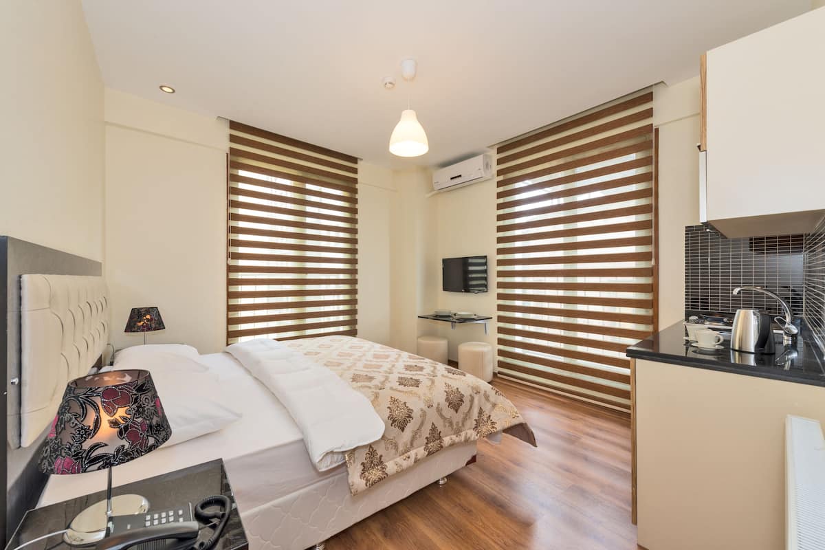 Ein Hotelzimmer mit Bett, Nachttischlampe, Nachttisch mit Telefon, kleinem Schreibtisch mit Stuhl, Wand-Fernseher und einer Küchenzeile.