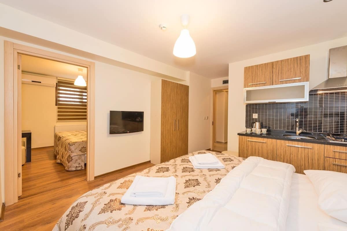 Ein modernes Hotelzimmer mit einem großen Bett, einem an der Wand befestigten Fernseher, einer Küchenzeile und einem durch eine offene Tür einsehbaren Badezimmer.