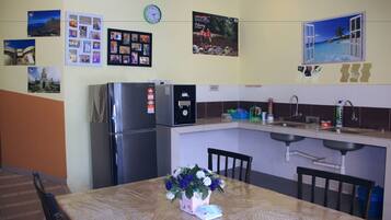 A kitchen with a refrigerator, sink, and a dining table with chairs. There are pictures on the wall and a clock.