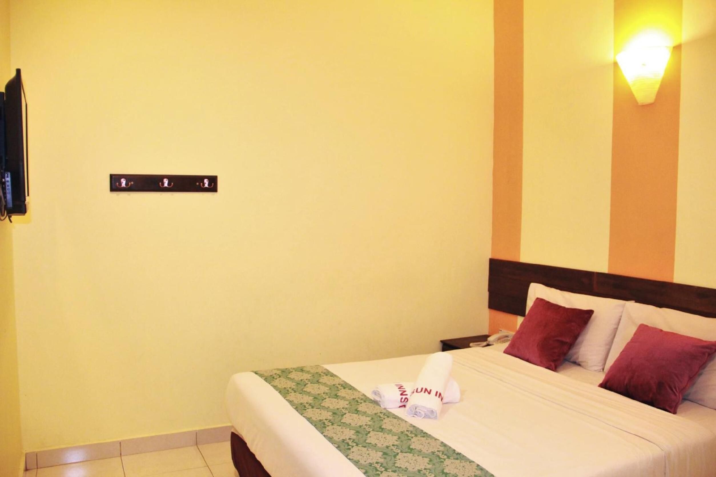Habitación de hotel con cama, almohadas, televisión montada en la pared y lámpara.
