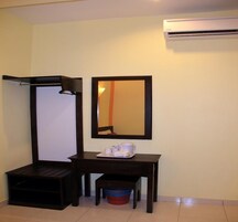 Una habitación pequeña con un banco de madera oscura, una mesa con una bandeja de artículos de aseo, un espejo y un equipo de aire acondicionado.
