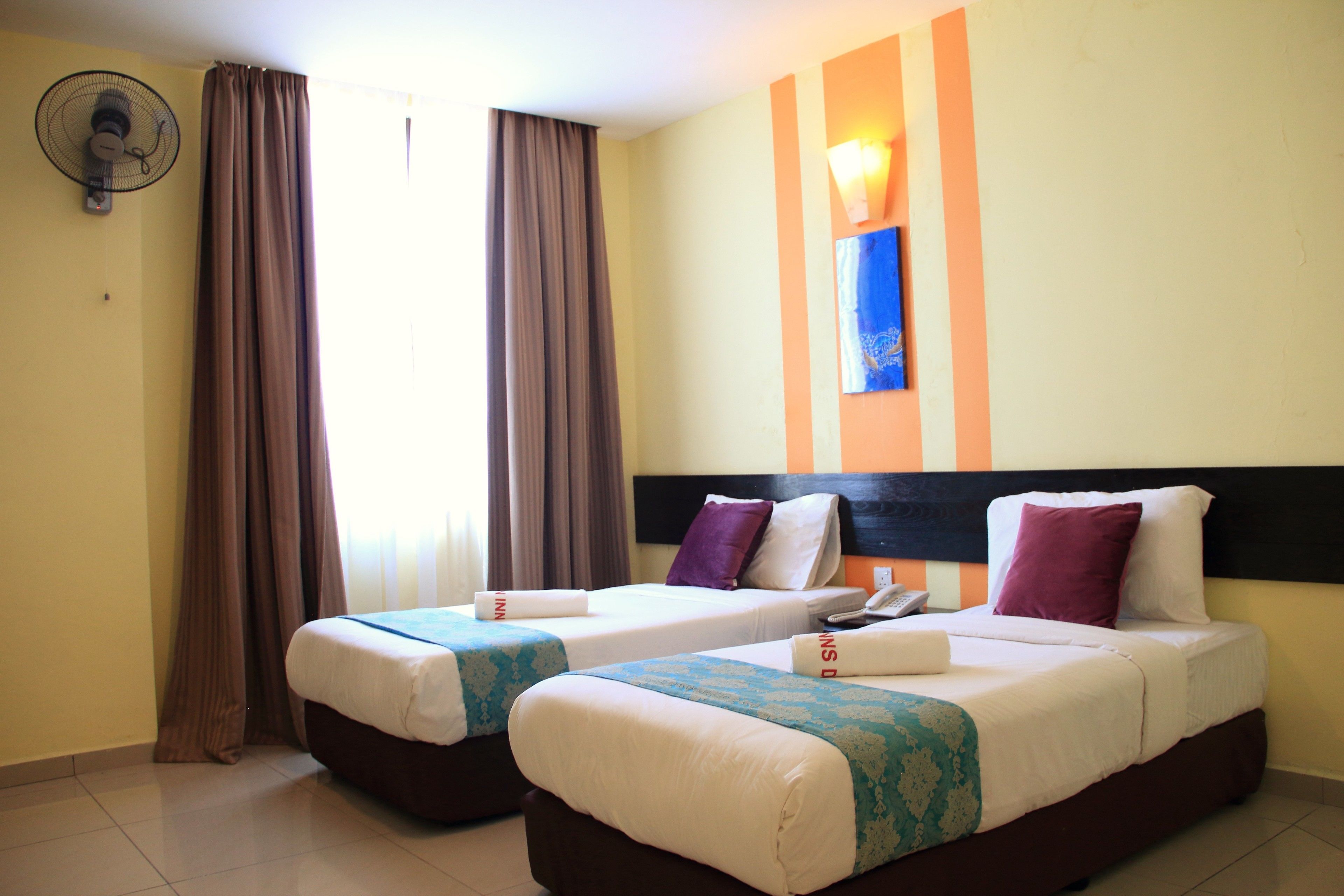 Habitación de hotel con dos camas individuales, un ventilador, un teléfono y un cuadro en la pared.