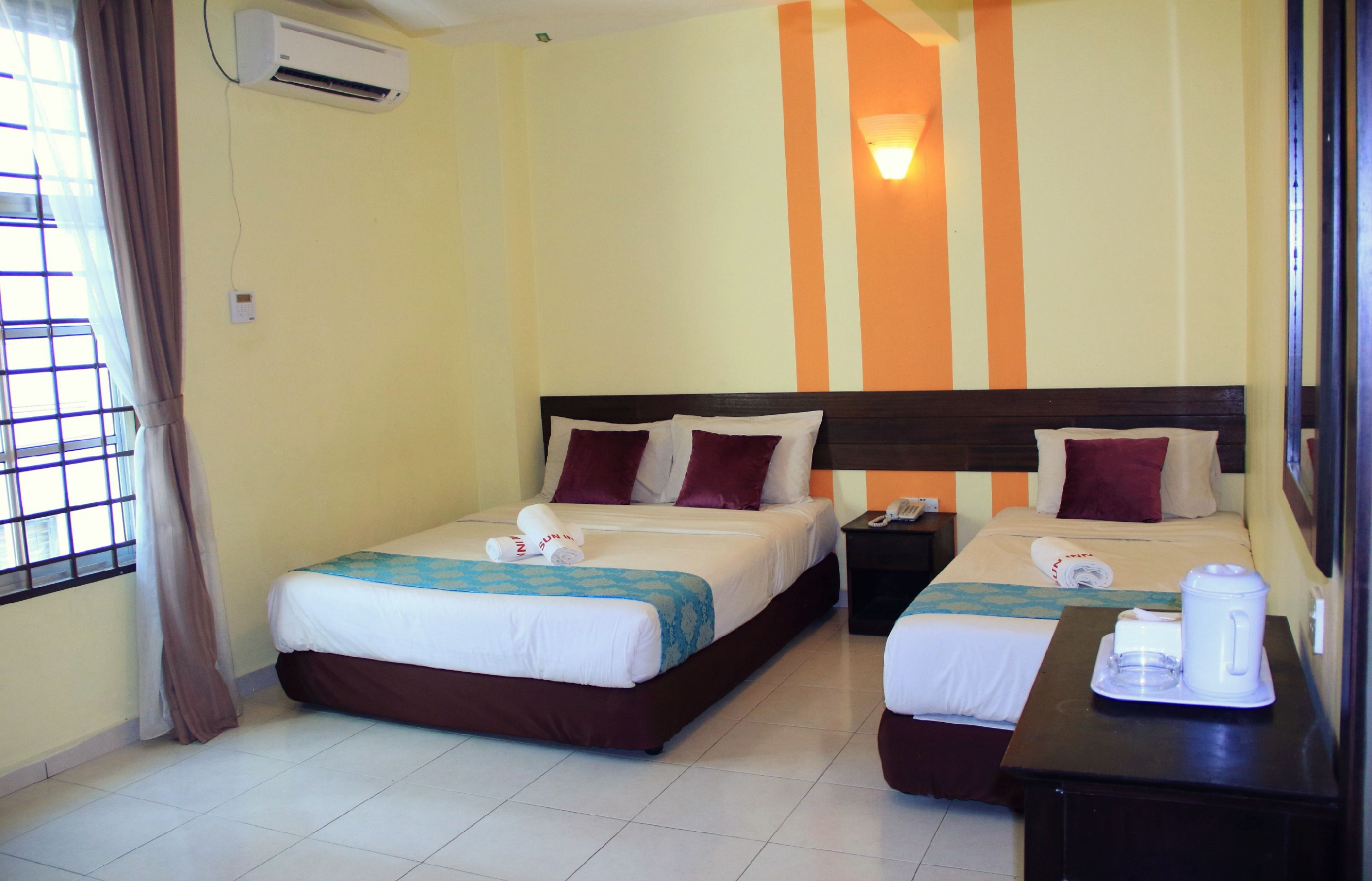 A hotel room with two beds, a nightstand, a coffee maker, and an air conditioning unit.