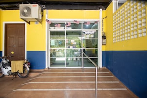 Fachada de edificio con pared amarilla y azul, una puerta marrón y una motocicleta estacionada afuera.