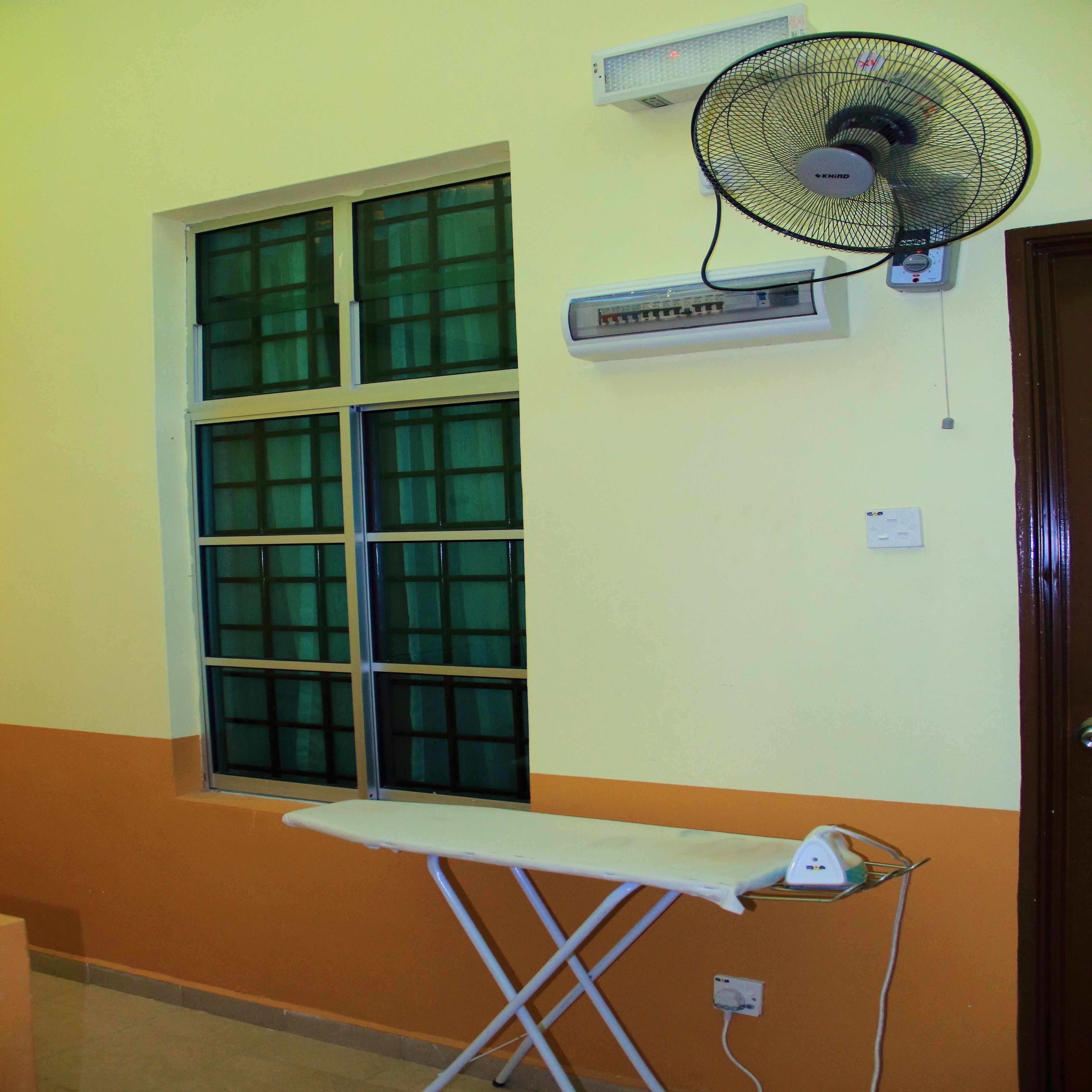 Quarto com janela, tábua de passar, ventoinha na parede e ar condicionado.