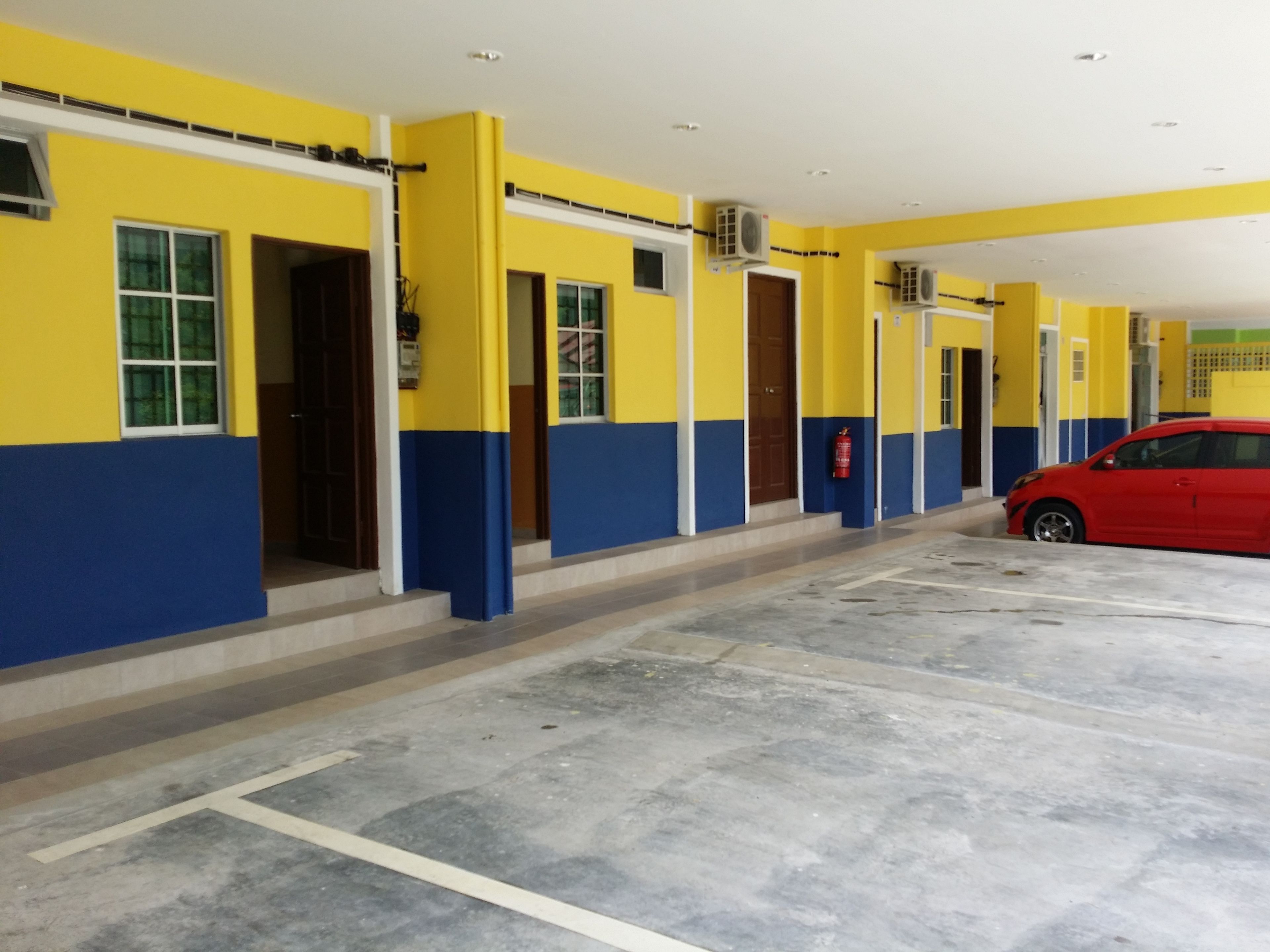 A building with yellow and blue exterior walls, a red car parked in the foreground, and multiple doors and windows.