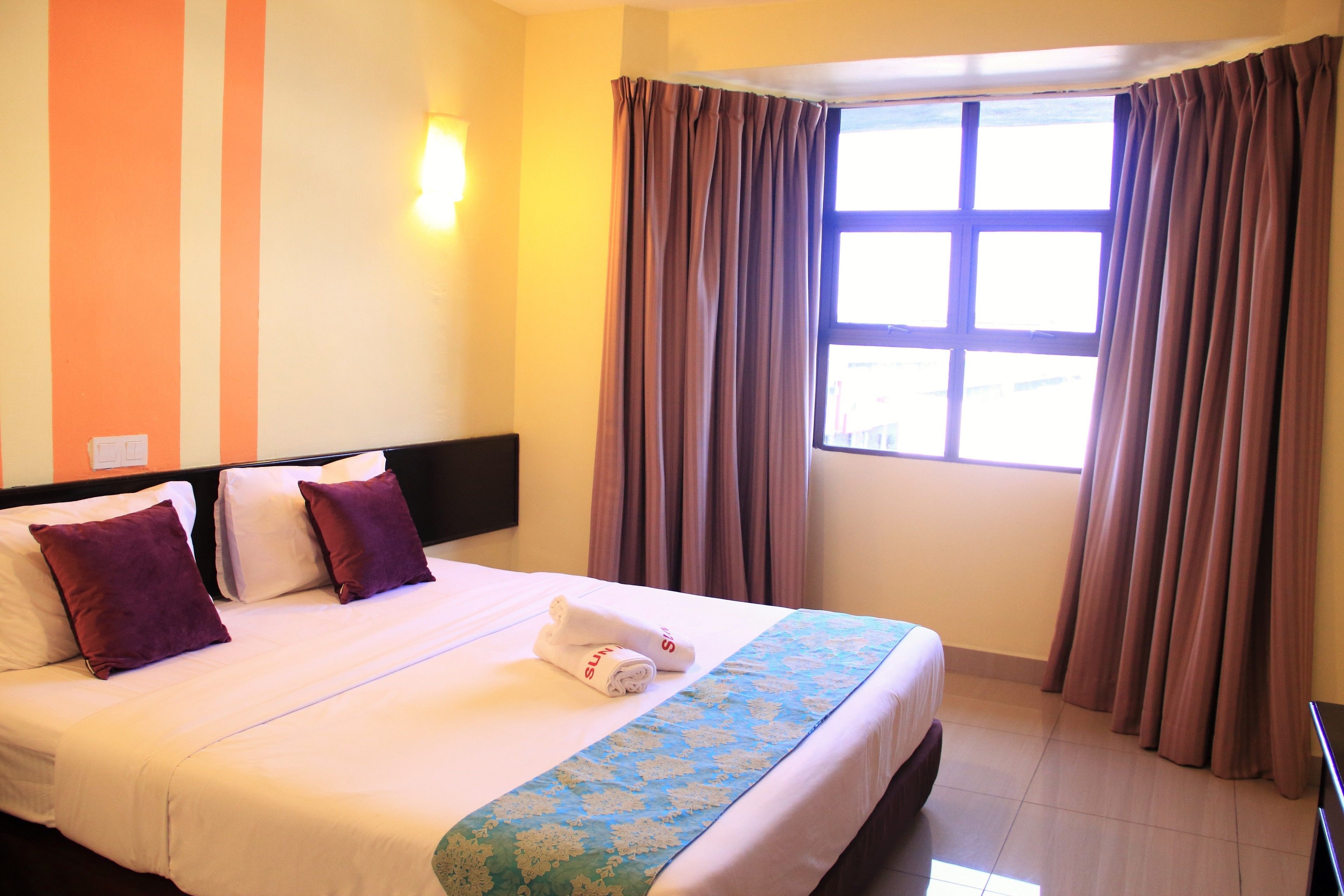 Una habitación de hotel con cama, almohadas, una ventana con cortinas y una pared a rayas.