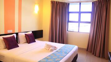 Una habitación de hotel con cama, almohadas, una ventana con cortinas y una pared a rayas.