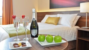 Een netjes gedekte tafel met een fles wijn, twee glazen en een bord met chocolade en appels in een hotelkamer.