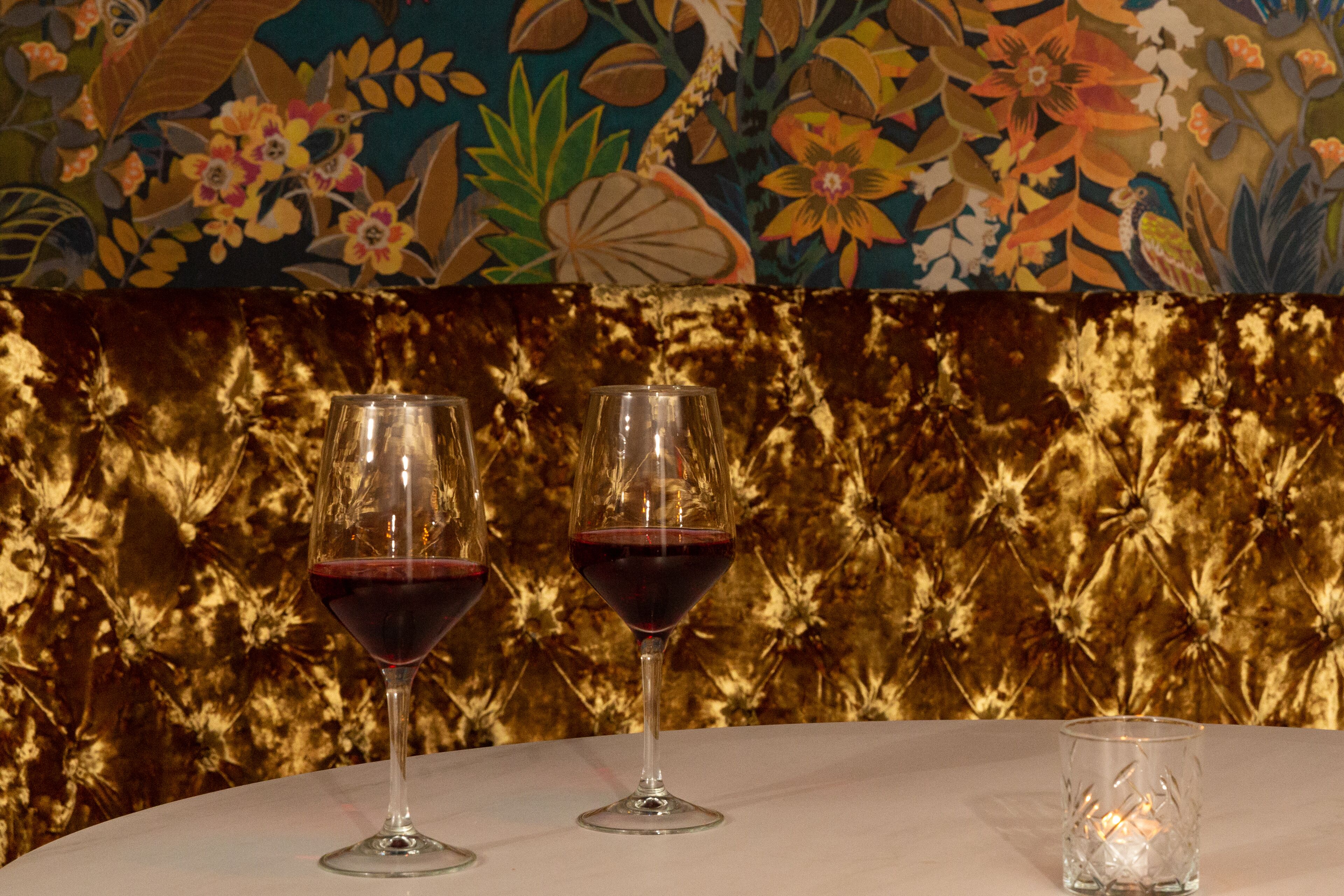Dos copas de vino sobre una mesa, con una pared decorativa al fondo.