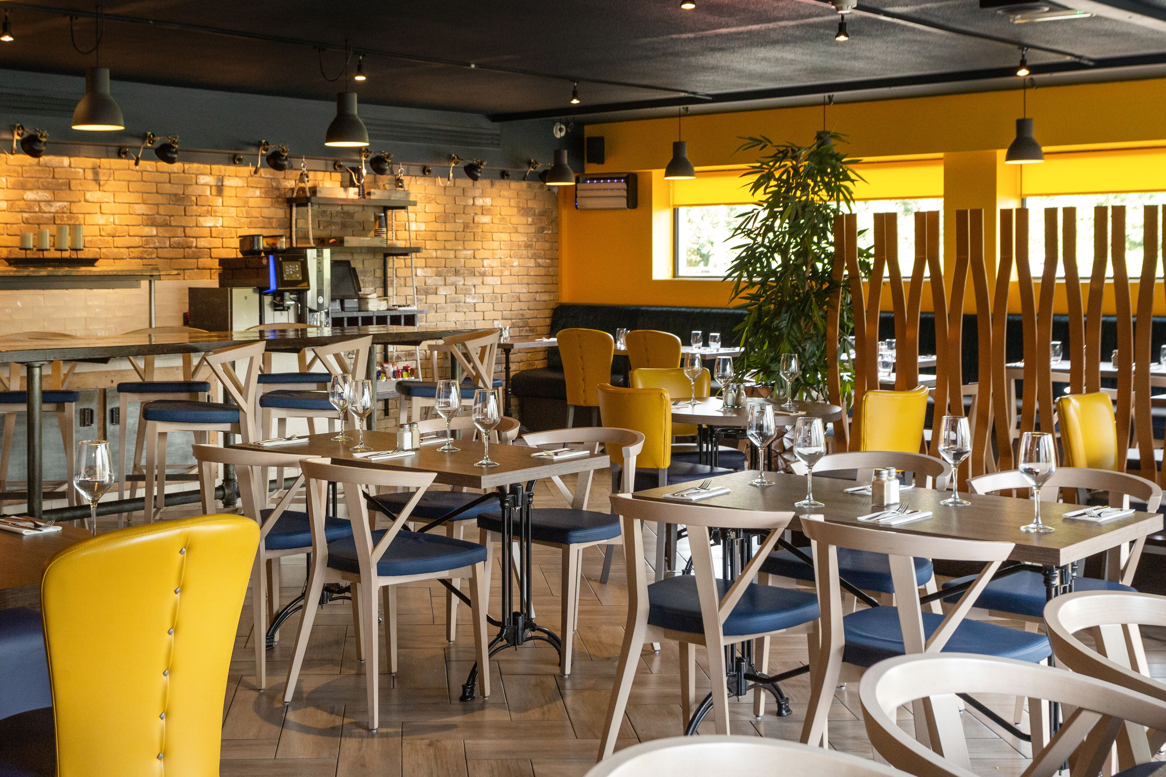 Un restaurant amb taules i cadires de fusta, una paret de maó i llums penjants.