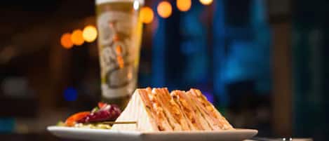 A sandwich on a plate with a glass of beer in the background.