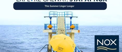 A boat deck with a Nox Hotel umbrella, a lifebuoy, and a railing.