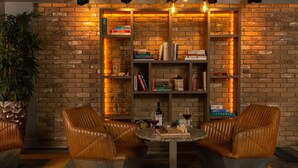 Een gezellige leeshoek met leren stoelen, een tafeltje en een boekenkast tegen een metselwerk muur.