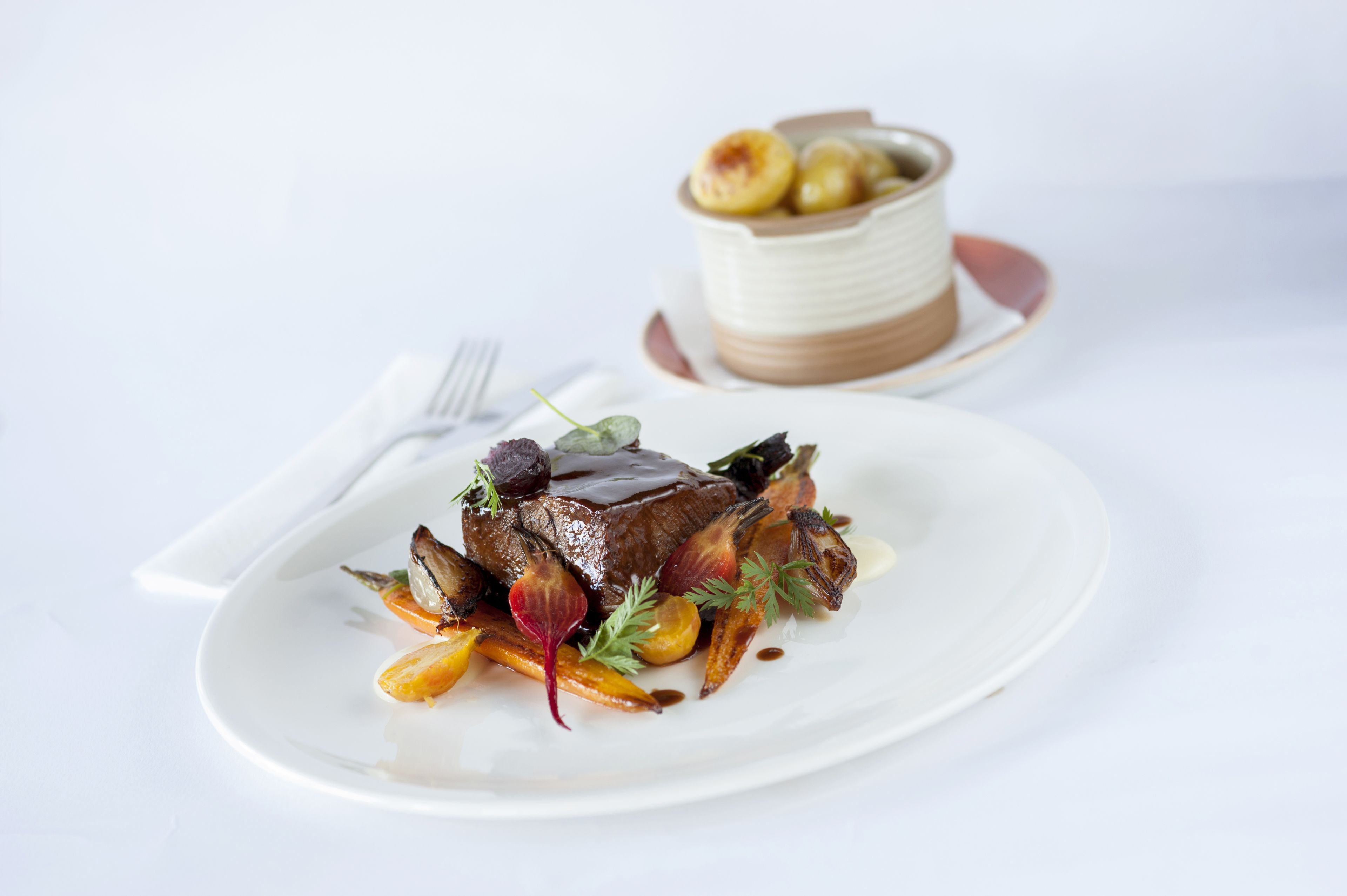 Un plato de comida con carne, verduras y un tazón pequeño de fruta al fondo.