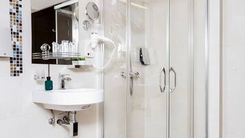 Un baño moderno con lavamanos blanco, espejo, cabina de ducha de vidrio y puerta de vidrio.