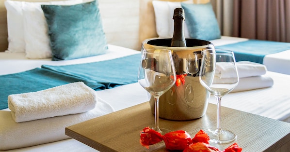 A bed with a wooden tray holding a champagne bottle, two wine glasses, and red flowers.