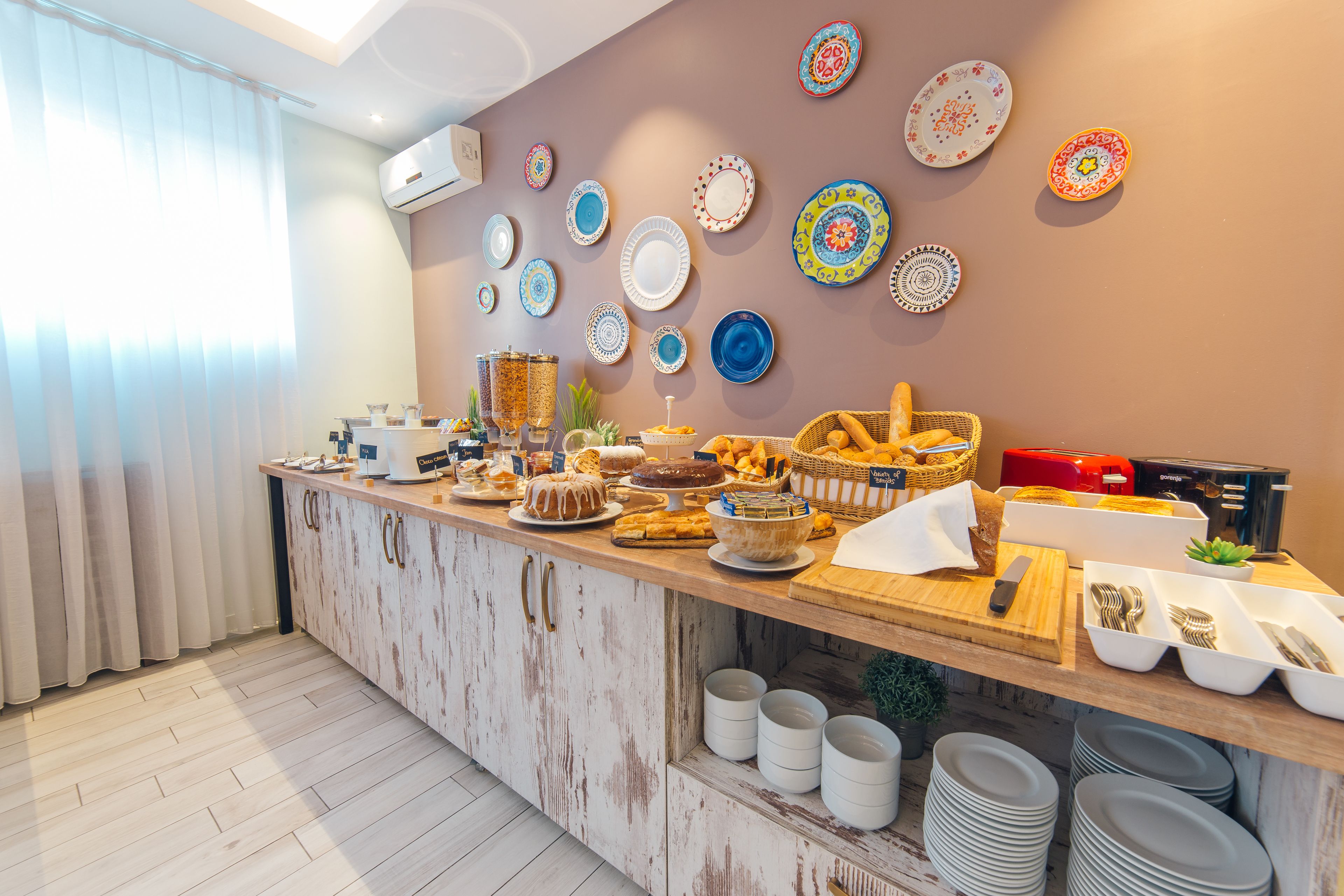 A breakfast buffet with various dishes, a wall decorated with plates, and a kitchen area with a wooden counter and cabinets.