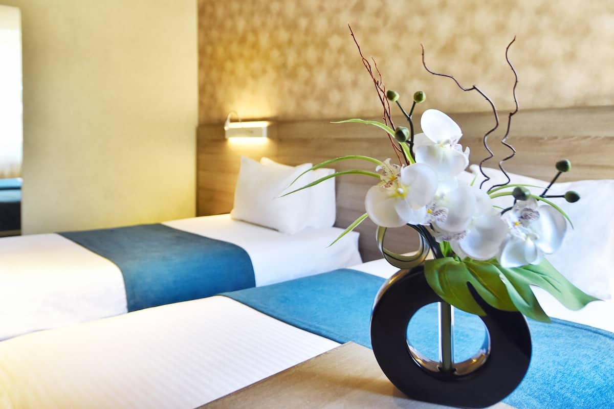 A hotel room with a bed, a bedside table with a vase of white flowers, and a blue and white striped blanket.