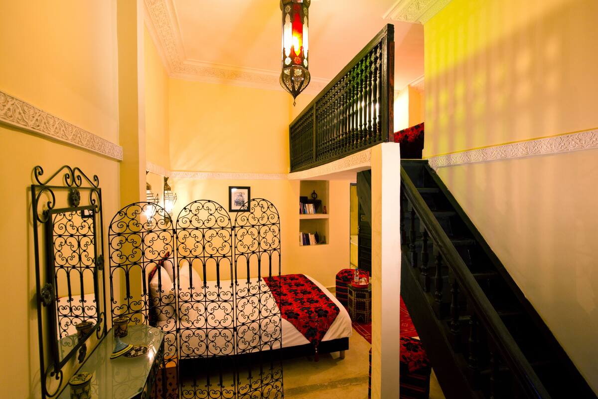 A bedroom with a bed, a nightstand, a dresser, a mirror, and a staircase.