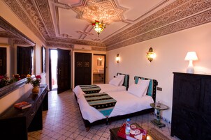 A hotel room with two beds, a dresser, a mirror, a chandelier, and decorative wall sconces.