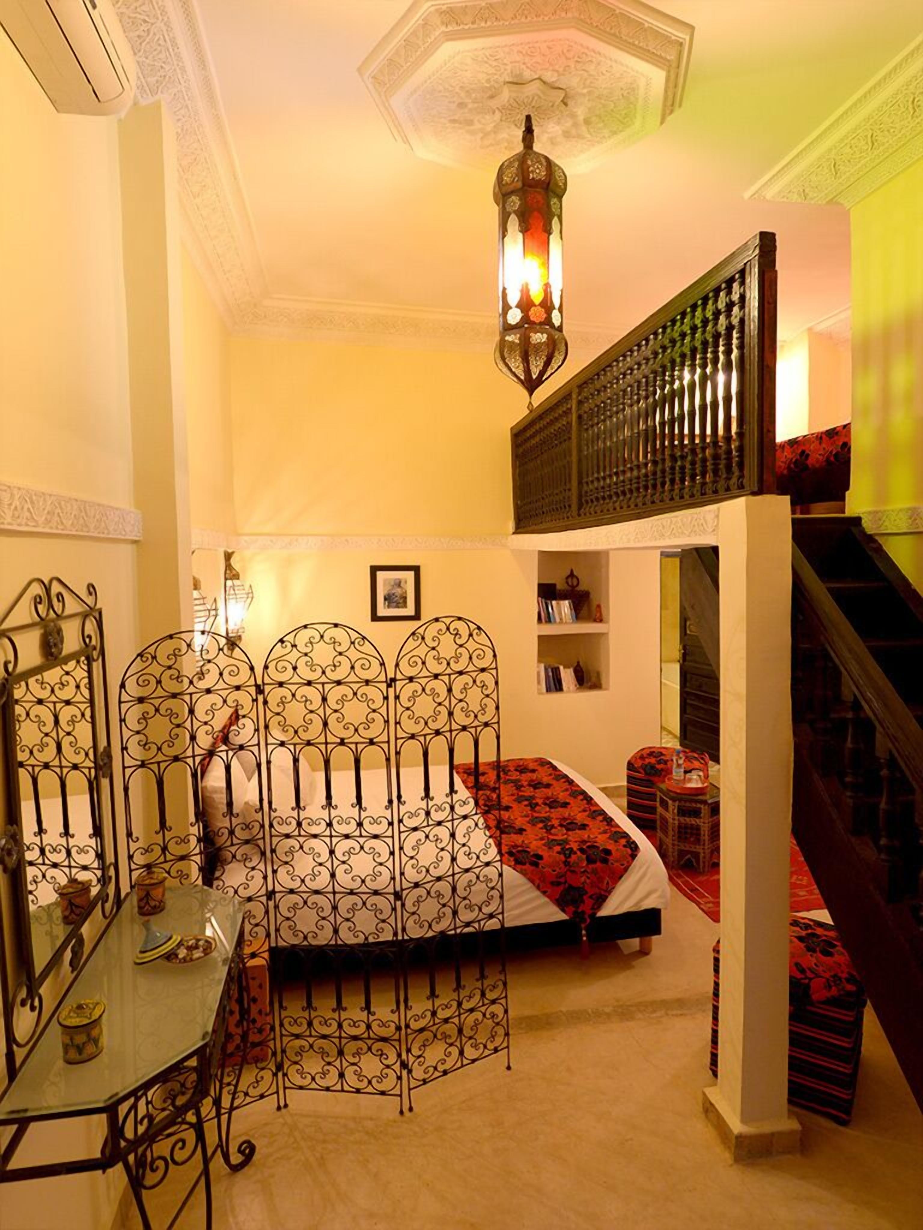 Quarto com cama, mesa de jantar, escada e luminária decorativa no teto.